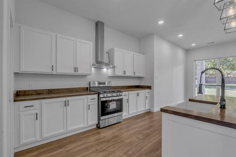 Kitchen with white cabinetry, wall chimney range hood, stainless steel gas range oven, and light hardwood / wood-style flooring