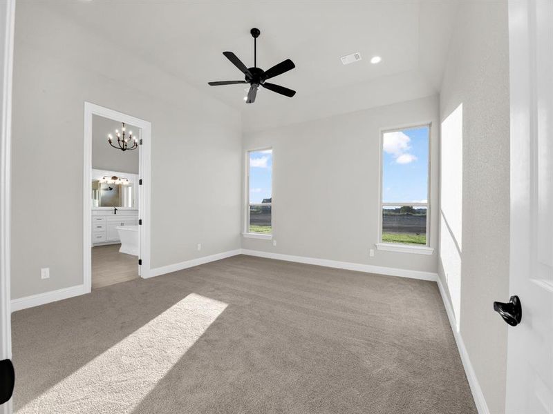 Unfurnished bedroom with carpet, ceiling fan with notable chandelier, multiple windows, and ensuite bath