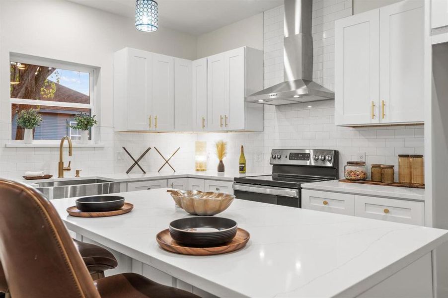 Kitchen with stainless steel range with electric cooktop, backsplash, white cabinetry, wall chimney exhaust hood, and decorative light fixtures