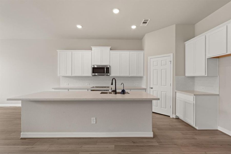 This light and bright kitchen features a large quartz island, white cabinets, a large sink overlooking your family room, recessed lighting, and beautiful backsplash.