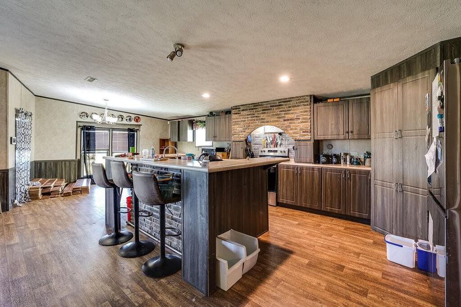 Kitchen with light hardwood / wood-style flooring, an island with sink, a textured ceiling, and appliances with stainless steel finishes