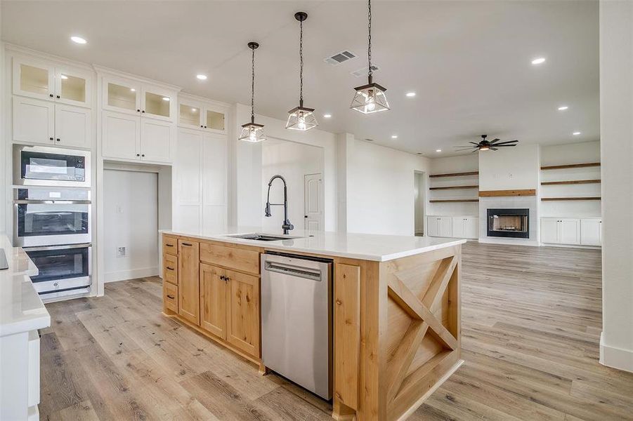 Kitchen featuring a tiled fireplace, stainless steel appliances, white cabinetry, an island with sink, and ceiling fan