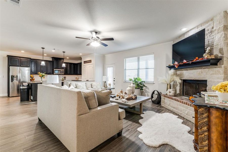 Living room with ceiling fan, a stone fireplace, crown molding, and dark hardwood / wood-style flooring