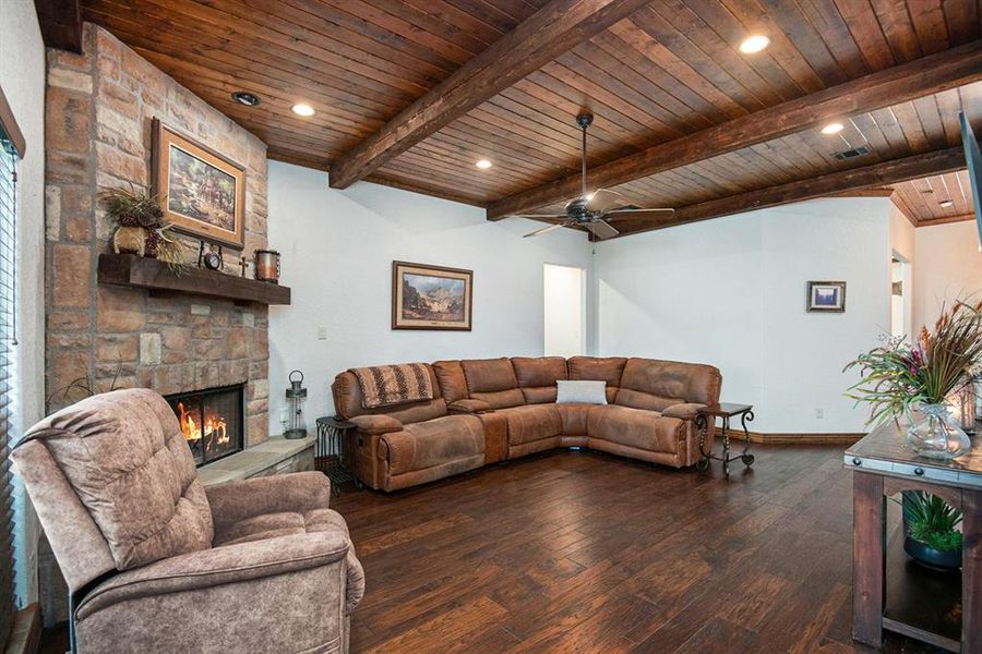 Living room with a fireplace, wood ceiling, ceiling fan, beam ceiling, and dark hardwood / wood-style floors