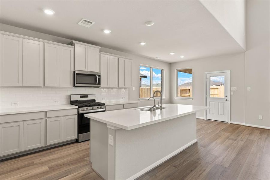 This light and bright kitchen features a large quartz island, white cabinets, a large sink overlooking your family room, recessed lighting, and beautiful backsplash.