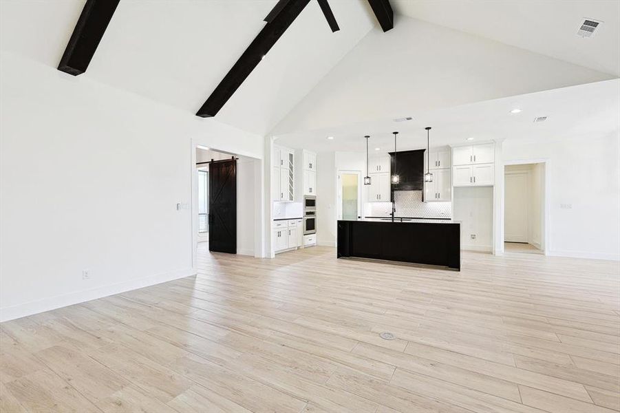 Unfurnished living room with high vaulted ceiling, beam ceiling, light hardwood / wood-style floors, and sink