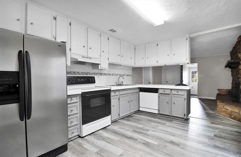 Kitchen featuring tasteful backsplash, white appliances, light wood-type flooring, and a textured ceiling