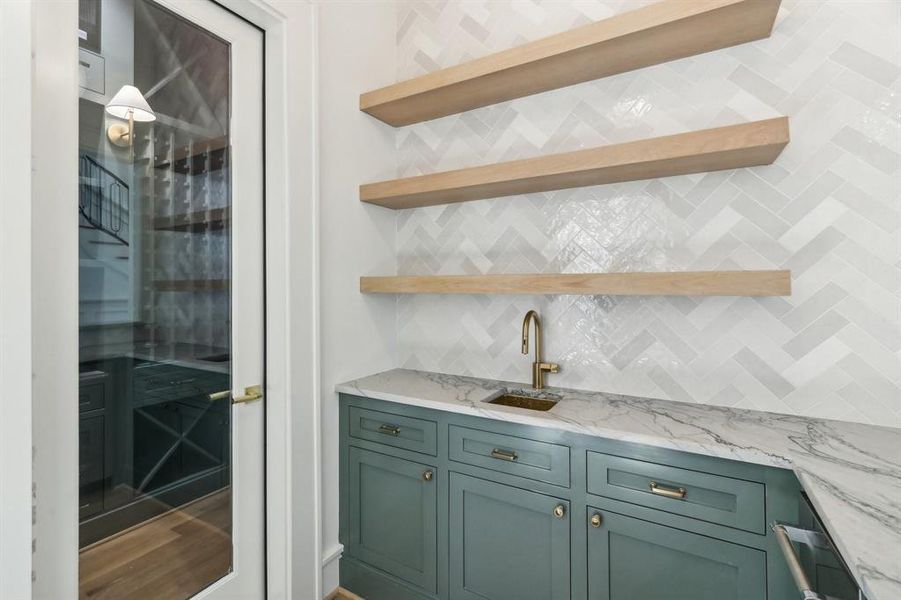 Behind the glass door is a conditioned wine room. There is an icemaker, a bar sink and plenty of storage in the wet bar for both functional items (below) and sexy glassware above.