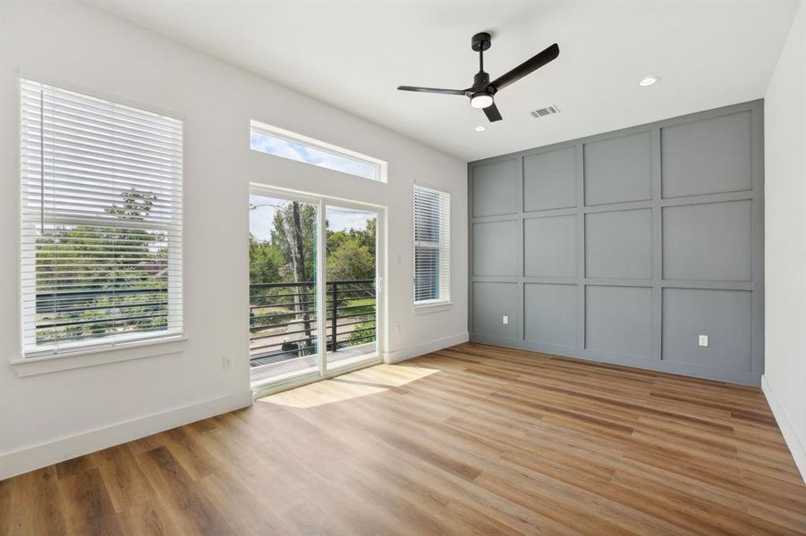 Primary bedroom with all wood flooring, tons of natural light, balcony, and a custom designed accent wall