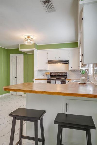 Kitchen featuring a kitchen breakfast bar, kitchen peninsula, white cabinets, and black range with electric cooktop