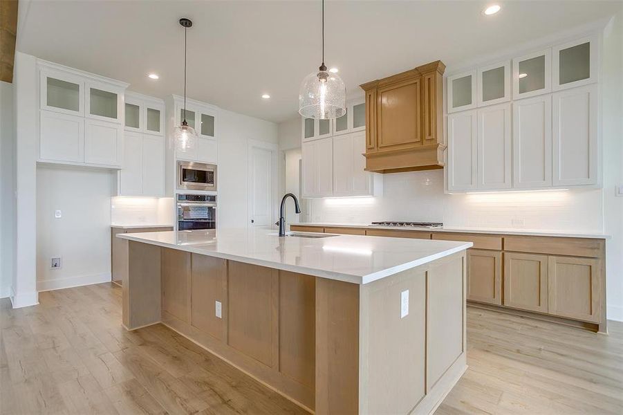 Kitchen with light hardwood / wood-style floors, a large island with sink, tasteful backsplash, and sink