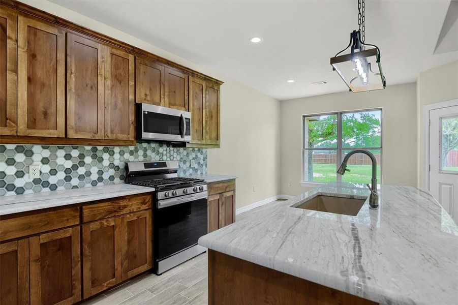 Kitchen with stainless steel appliances, hanging light fixtures, decorative backsplash, sink, and light quartzite countertops