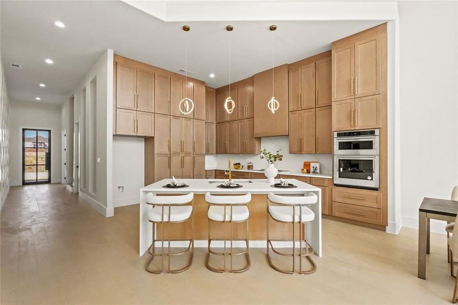 Kitchen featuring stainless steel double oven, an island with sink, sink, a breakfast bar, and decorative light fixtures