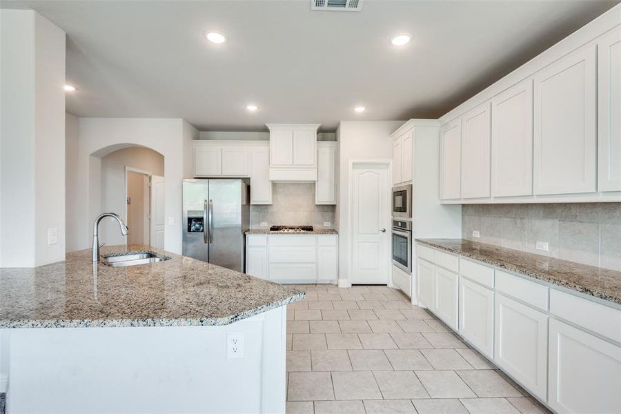 Kitchen featuring stainless steel appliances, white cabinets, and light stone counters