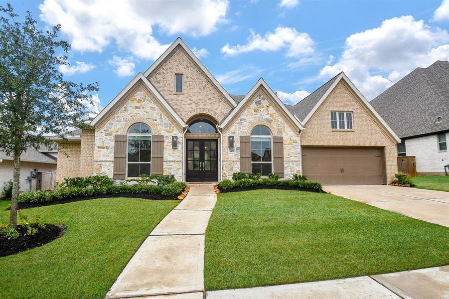 Single-story home featuring a brick and stone exterior, an arched entryway, a three-car garage, and well-manicured landscaping.