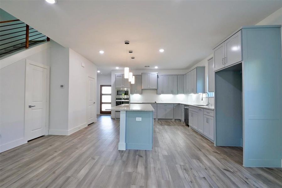 Kitchen featuring appliances with stainless steel finishes, hanging light fixtures, a kitchen island, and light hardwood / wood-style flooring