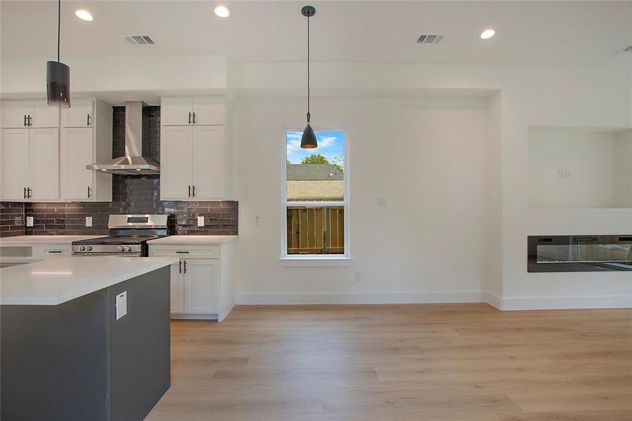 Kitchen with wall chimney range hood, white cabinets, light wood-type flooring, and stainless steel stove