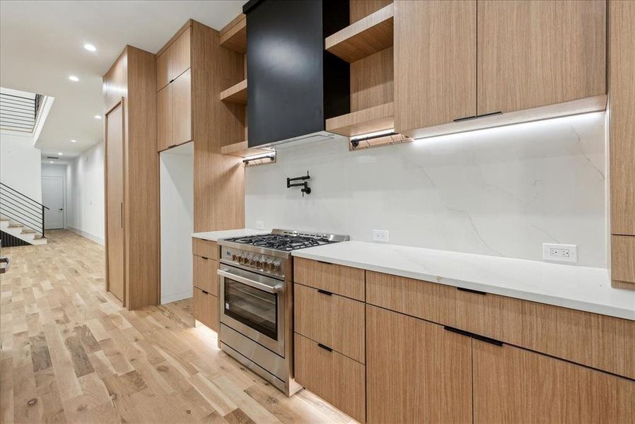 Kitchen featuring light stone counters, light brown cabinets, light hardwood / wood-style flooring, and high end range