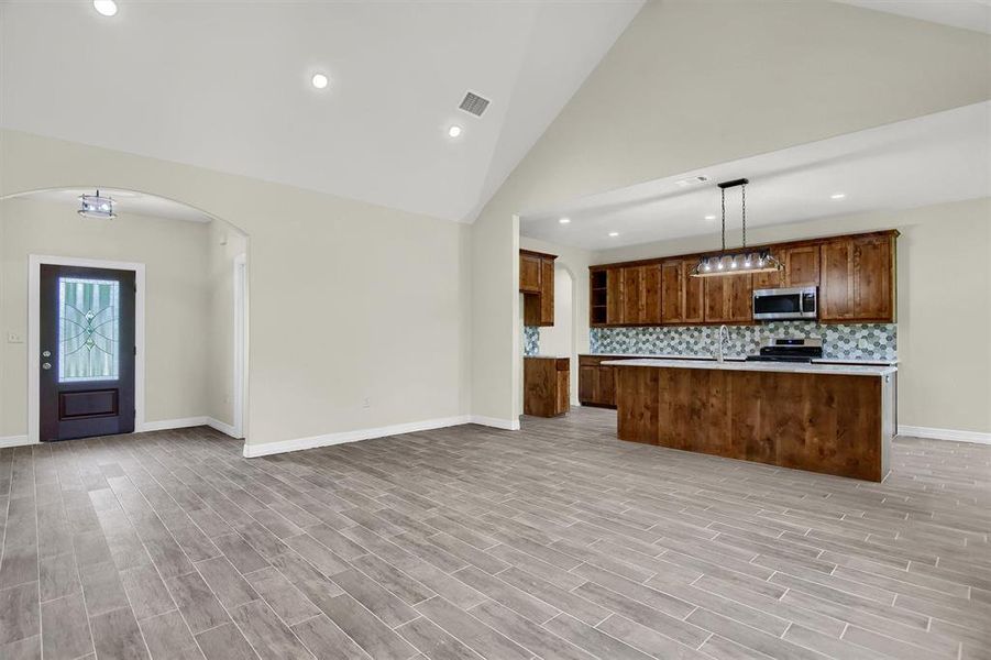 Kitchen featuring range, a center island, backsplash, hanging light fixtures, and high vaulted ceiling