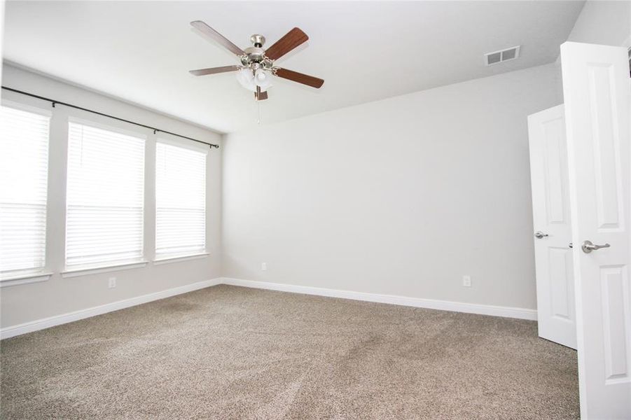 Primary bedroom with ensuite bathroom, large windows, and a ceiling fan