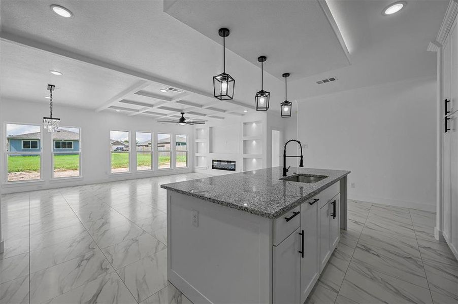 Kitchen with decorative light fixtures, coffered ceiling, a kitchen island with sink, and sink