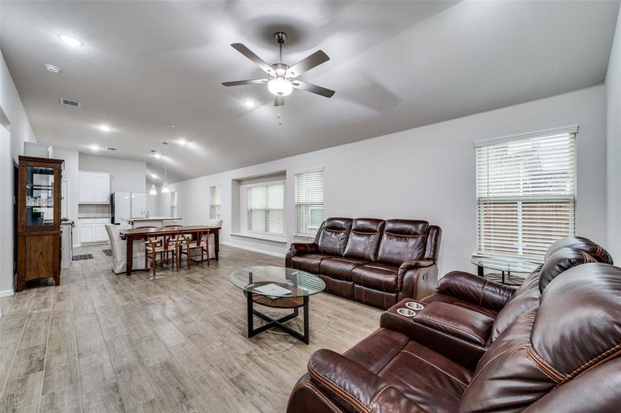 Living room with a wealth of natural light, light hardwood / wood-style flooring, ceiling fan, and vaulted ceiling