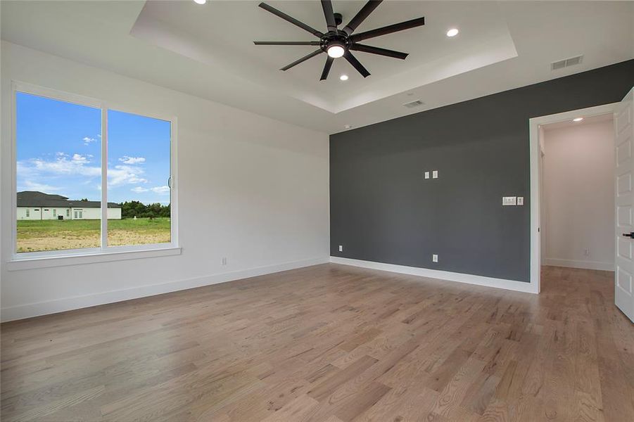 Empty room with ceiling fan, light hardwood / wood-style flooring, and a tray ceiling