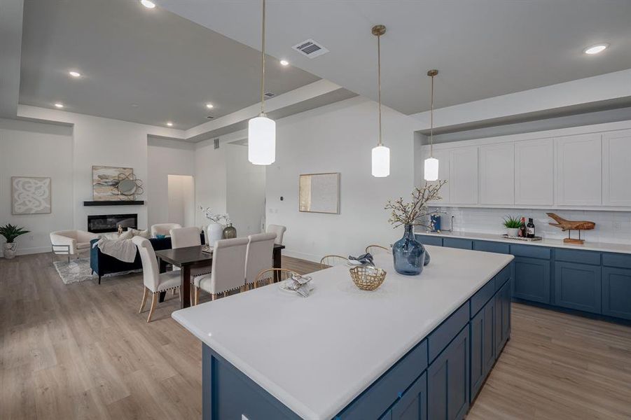 Kitchen with blue cabinetry, decorative light fixtures, light hardwood / wood-style floors, a kitchen island, and decorative backsplash