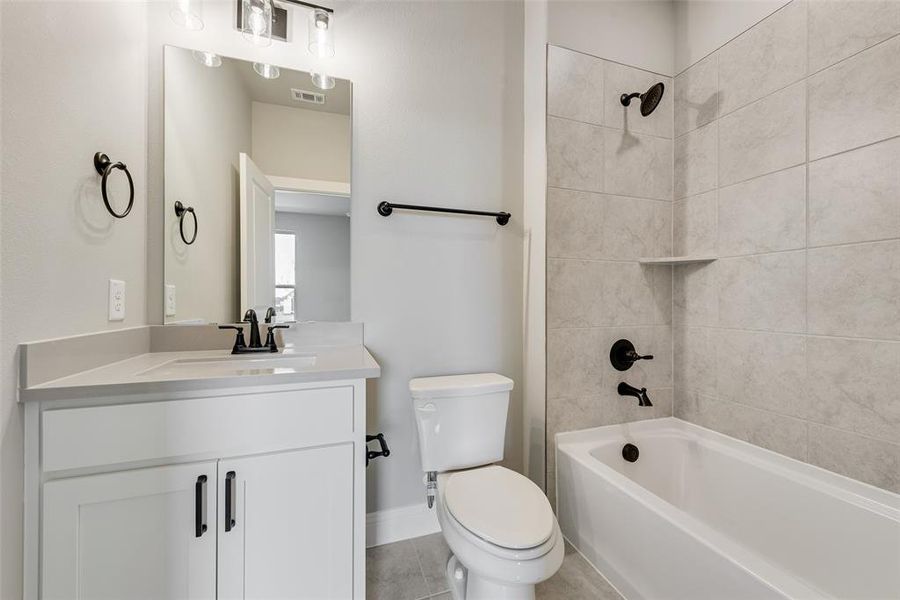 Full bathroom featuring tile patterned flooring, tiled shower / bath, vanity, and toilet