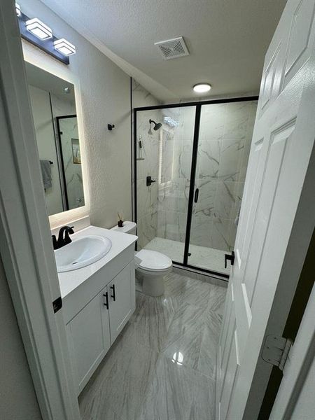 Bathroom with tile flooring, a textured ceiling, a shower with shower door, large vanity, and toilet