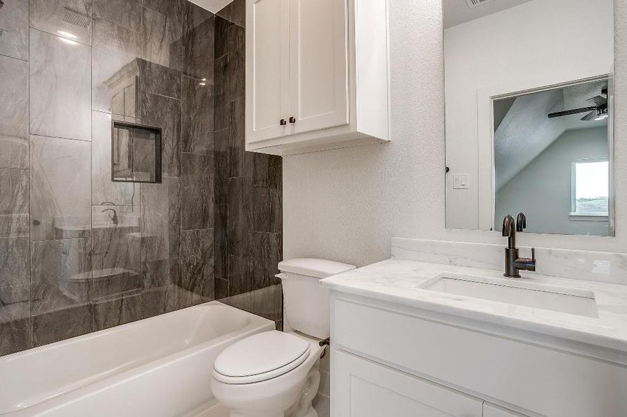 Full bathroom featuring vanity, toilet, tiled shower / bath, lofted ceiling, and ceiling fan