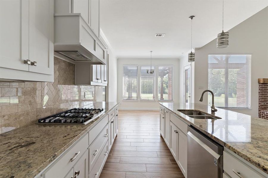 Kitchen with decorative light fixtures, custom exhaust hood, sink, appliances with stainless steel finishes, and backsplash