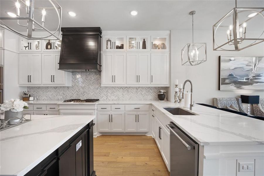 Kitchen featuring custom exhaust hood, white cabinetry, stainless steel appliances, sink, and decorative light fixtures