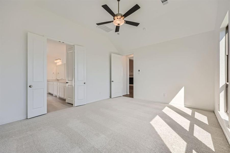 Unfurnished bedroom featuring light carpet, ensuite bath, vaulted ceiling, and ceiling fan