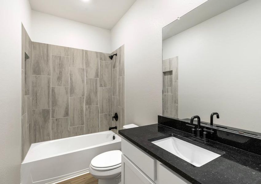 Secondary bathroom with black countertops and a dual shower and tub.