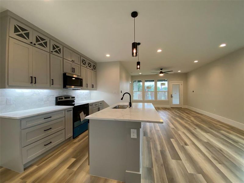 Kitchen with hardwood / wood-style floors, appliances with stainless steel finishes, sink, ceiling fan, and a center island with sink