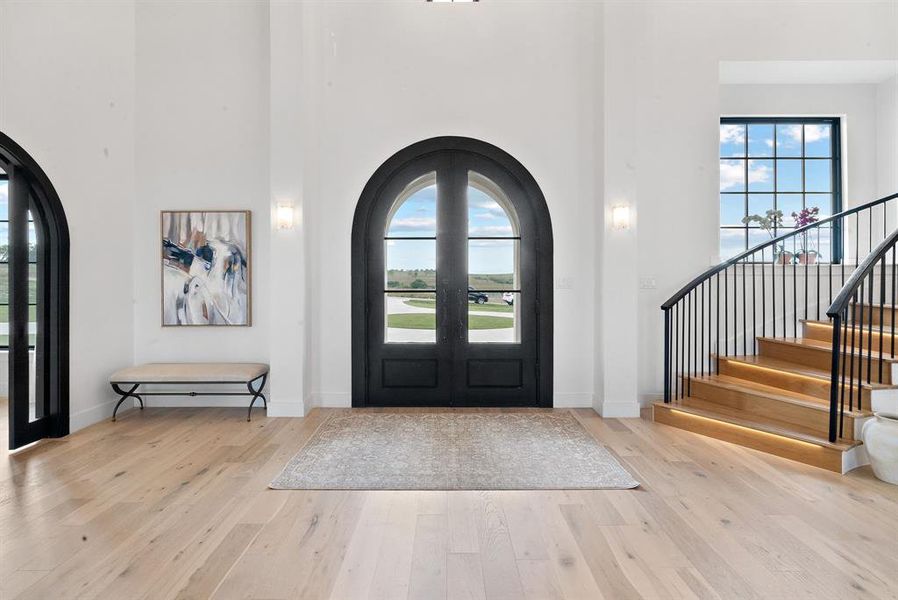 Foyer entrance featuring light hardwood / wood-style floors, french doors, and a towering ceiling