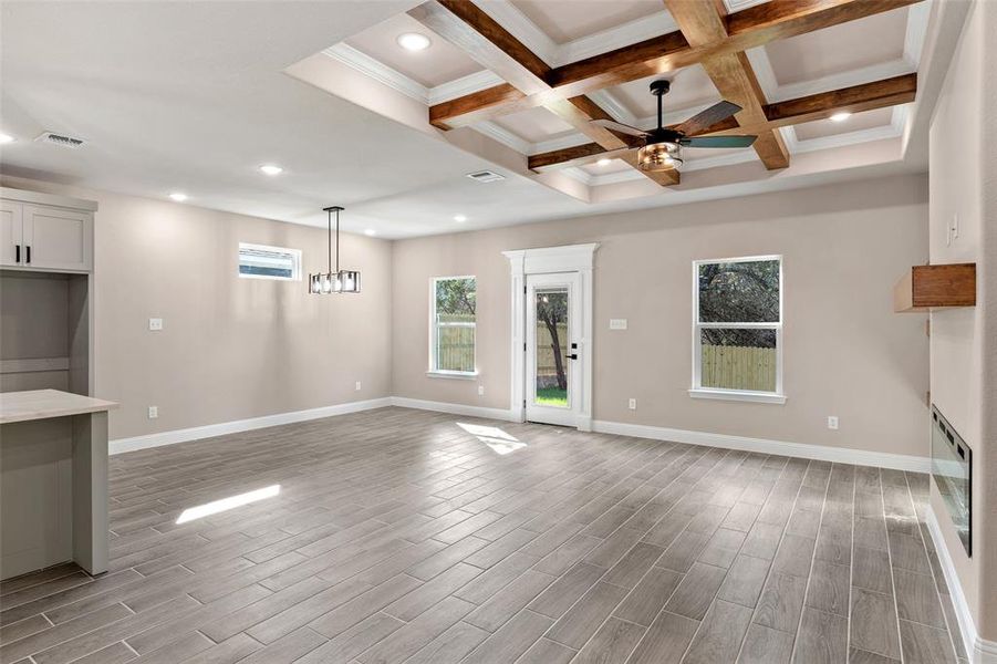 Unfurnished living room featuring beamed ceiling, coffered ceiling, light wood-type flooring, and ceiling fan with notable chandelier