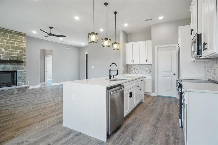 Kitchen featuring a stone fireplace, sink, light wood-type flooring, and an island with sink