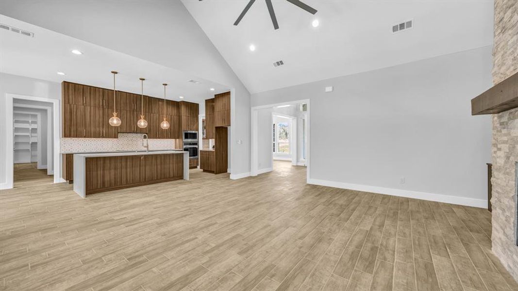 Unfurnished living room with light wood-type flooring, high vaulted ceiling, ceiling fan, a stone fireplace, and sink