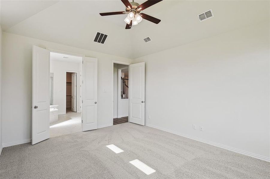 Unfurnished bedroom featuring light carpet, vaulted ceiling, ensuite bathroom, and ceiling fan