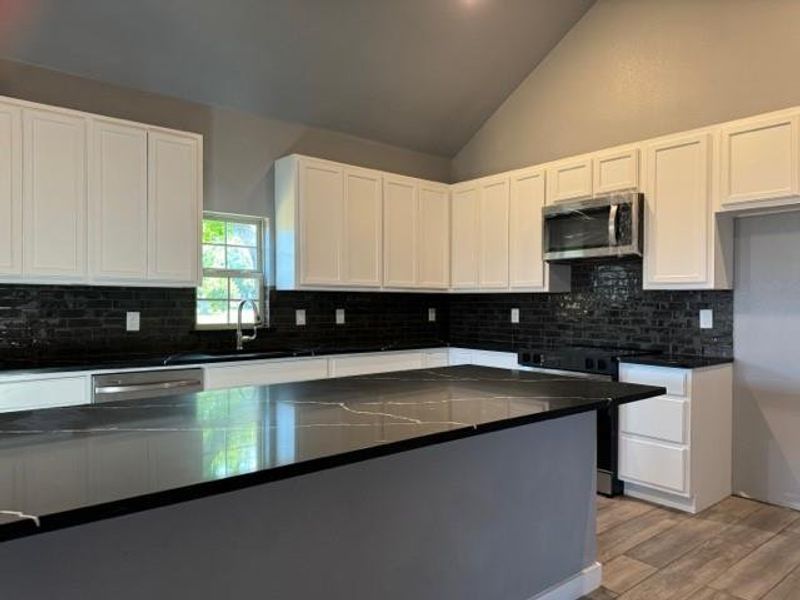 Kitchen featuring stainless steel appliances, white cabinets, and backsplash