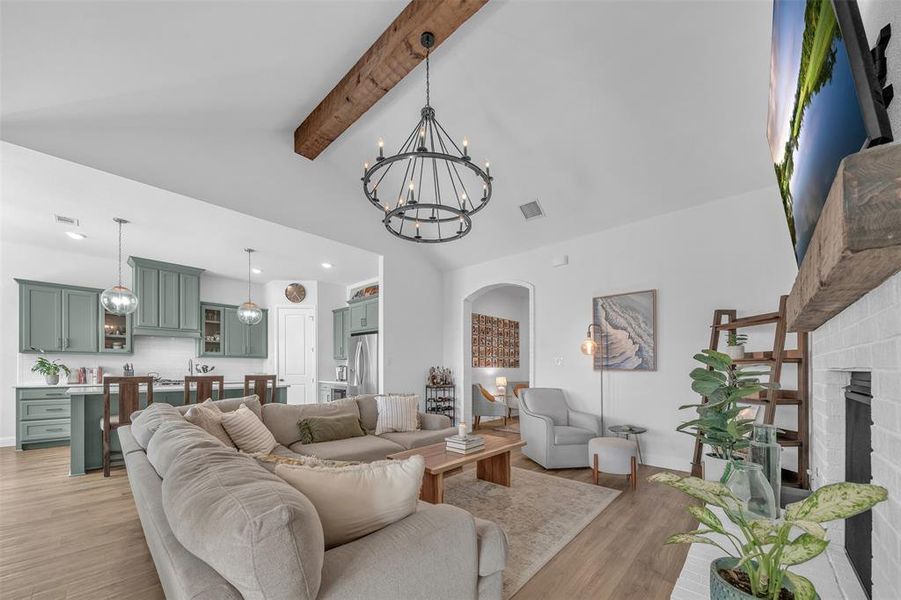 Living room featuring light hardwood / wood-style floors, beamed ceiling, an inviting chandelier, high vaulted ceiling, and a brick fireplace