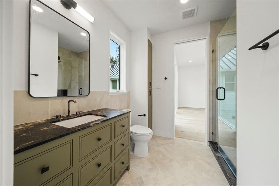 This image shows a modern bathroom, part of an upstairs extra bedroom, featuring Brazilian slate tile, a spacious walk-in shower, and a sleek vanity.