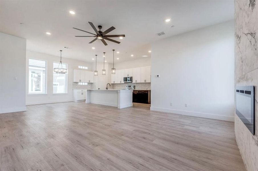 Unfurnished living room featuring heating unit, ceiling fan, sink, and light hardwood / wood-style floors