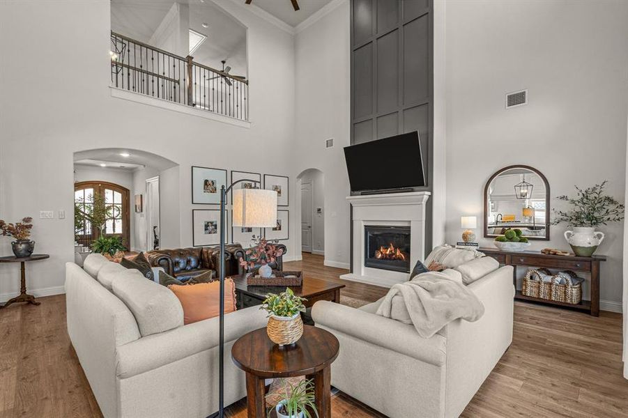 Living room featuring crown molding, ceiling fan, light wood-type flooring, and a high ceiling