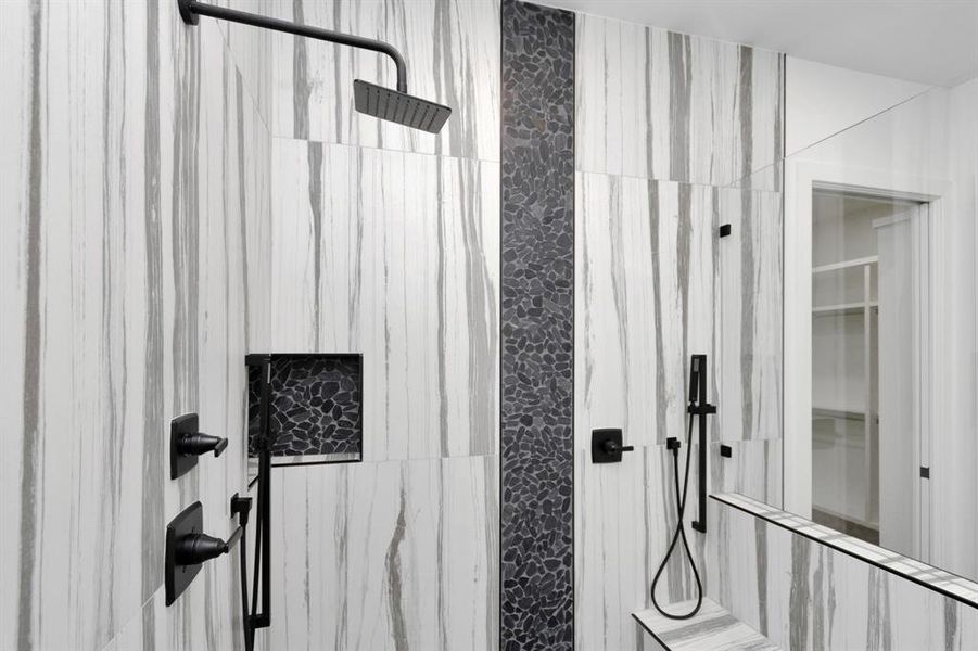 A beautigul walk-in shower that includes a rainfall shower head, a hand shower, and a built-in niche for toiletries. The fixtures are finished in matte black, and there's a glass partition with a glass door.