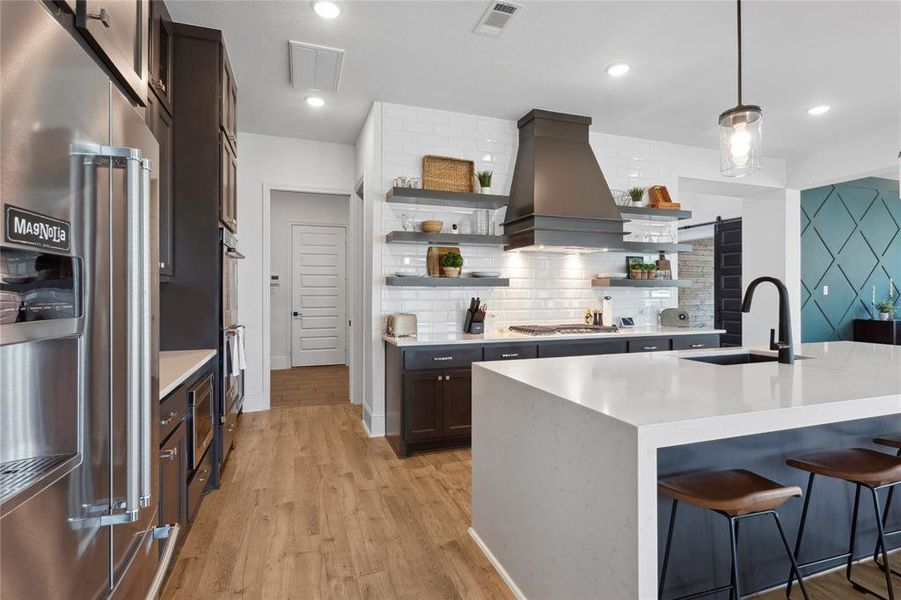 Modern vent hood and floating shelves conceal the walk-in pantry and laundry room tucked behind