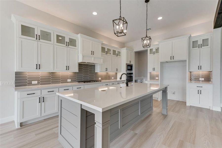 Kitchen with an island with sink, stainless steel appliances, backsplash, and white cabinetry