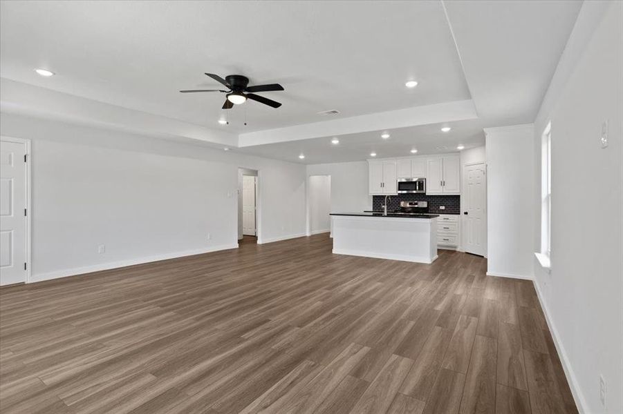 Unfurnished living room featuring hardwood / wood-style flooring, a tray ceiling, sink, and ceiling fan